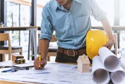 A man in a blue shirt writing construction plans