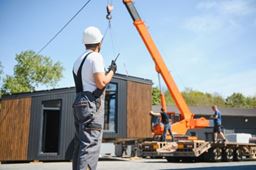 A construction worker on site with a modular home on a crane