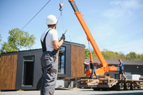 A construction worker on site with a modular home on a crane