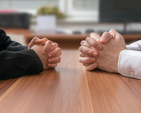 picture of two people sitting at a desk with their own hands interlocked ready for a discussion